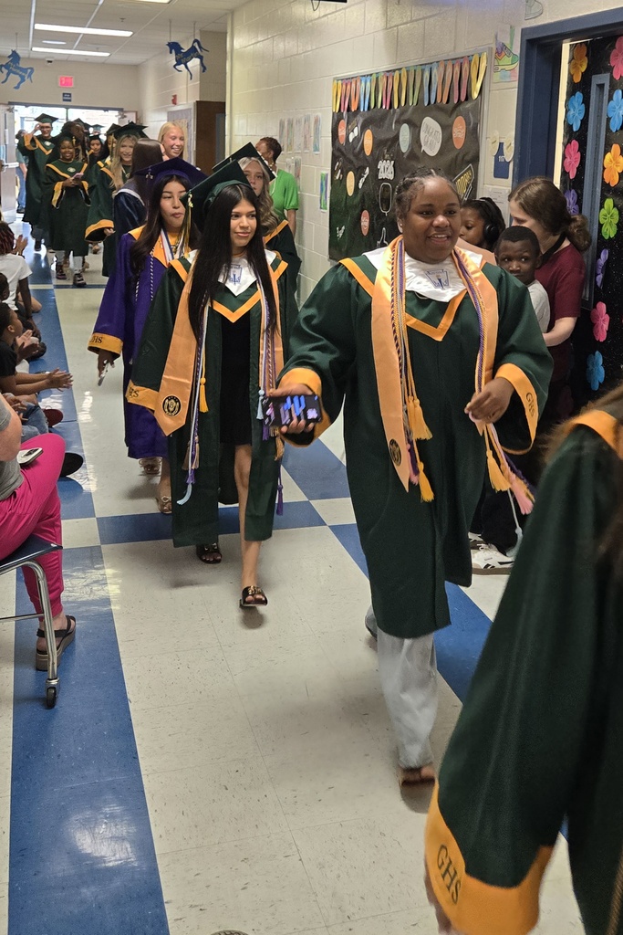 Seniors (in cap and gown) walking in elementary hall