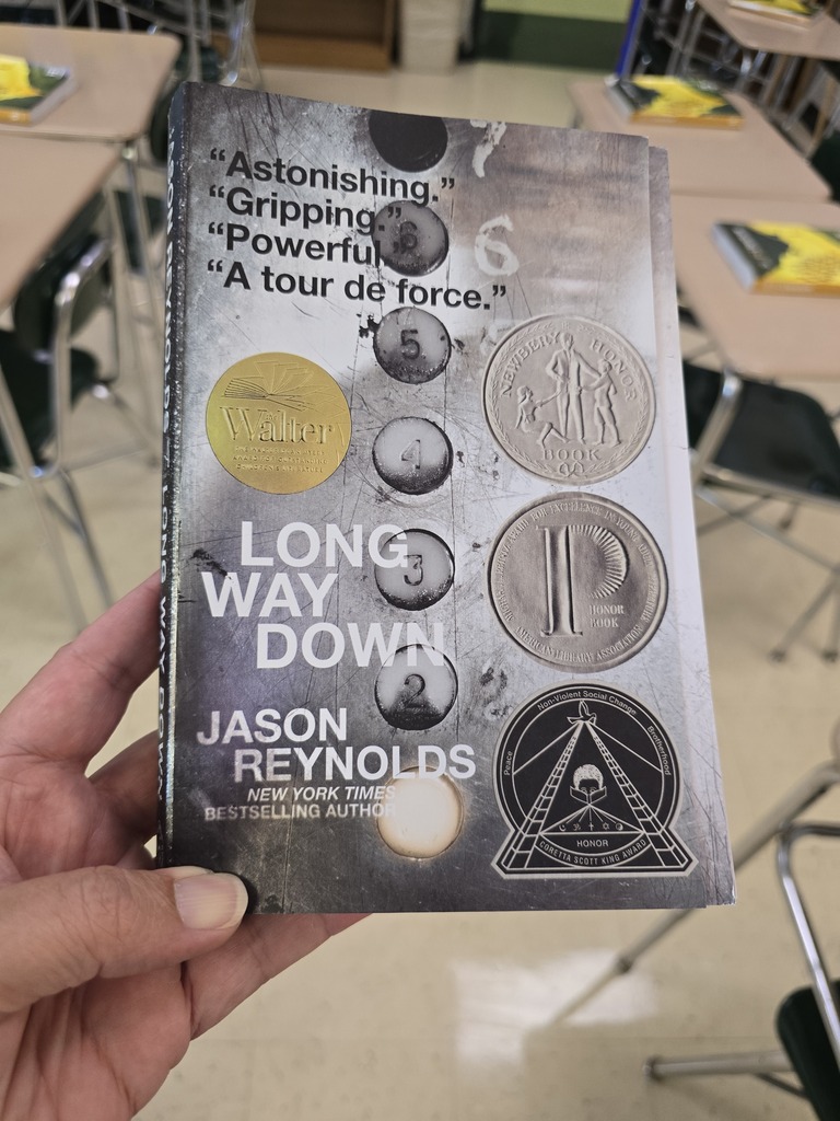 A teacher holds a copy of the book "Long Way Down" by Jason Reynolds