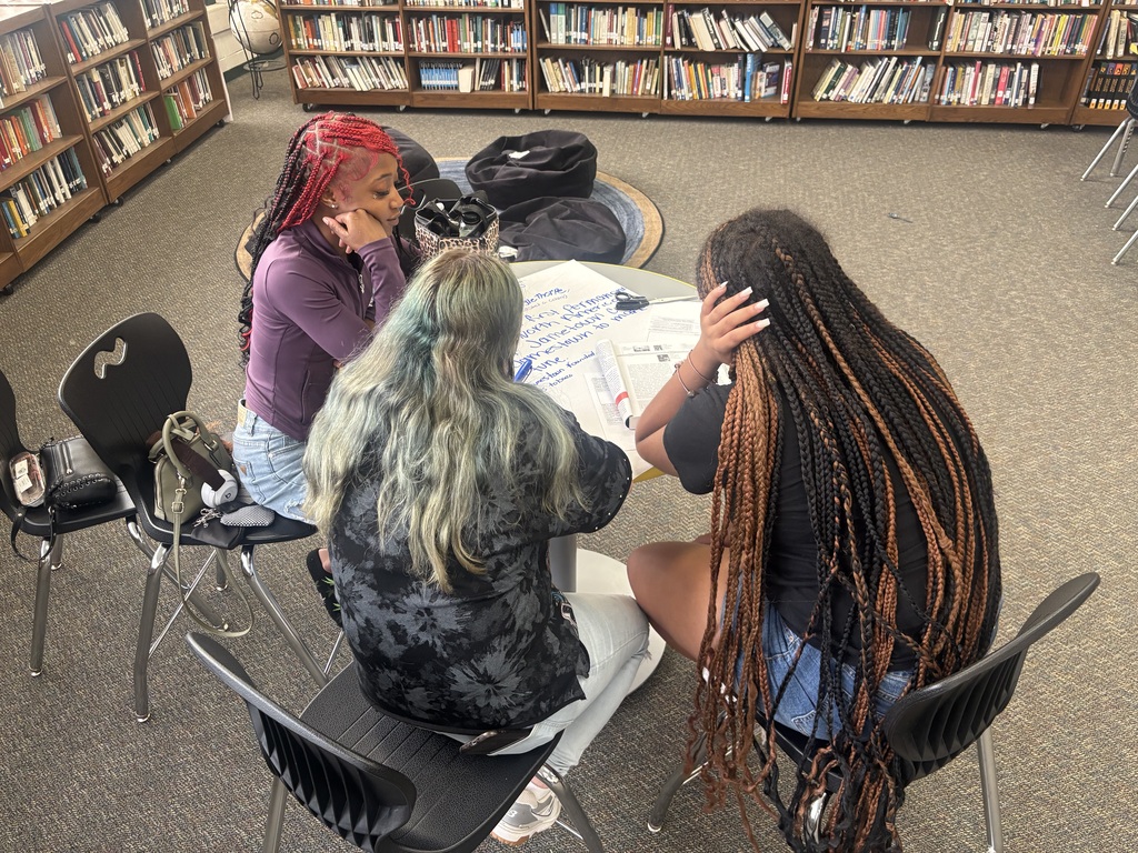 A group of students writes on their poster with reference to their texts.