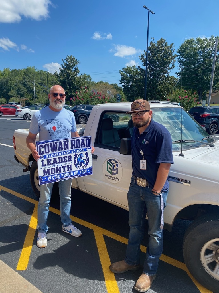two men in front of white truck labeled GSCS Schools holding a "Cowan Road Leader of the Month" sign