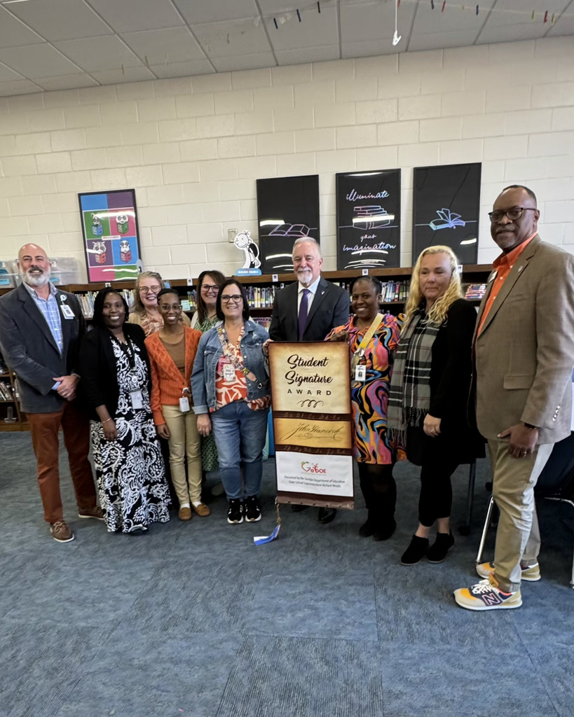 A group of educators and officials standing together in a school library, posing with a banner that reads "Student Signature Award" presented by the Georgia Department of Education.