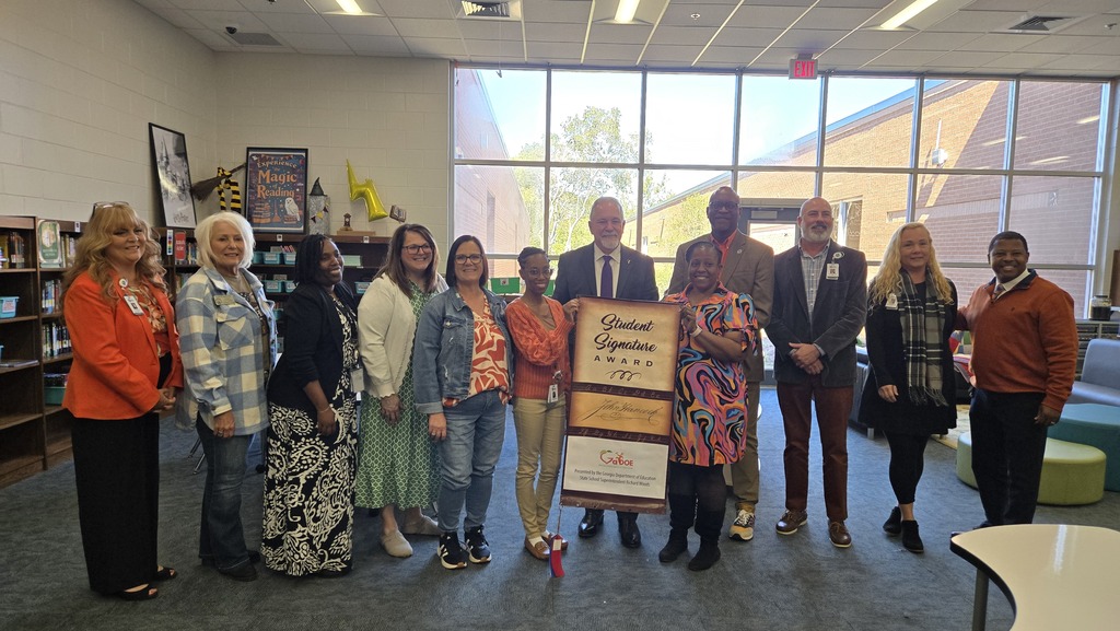 Group of ten attendees posing in a school library with the Georgia Department of Education "Student Signature Award" banner.