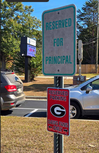 Sign reading "reserved for principal" with a new sign added below "Reserved Parking Dawgs Fans Only"