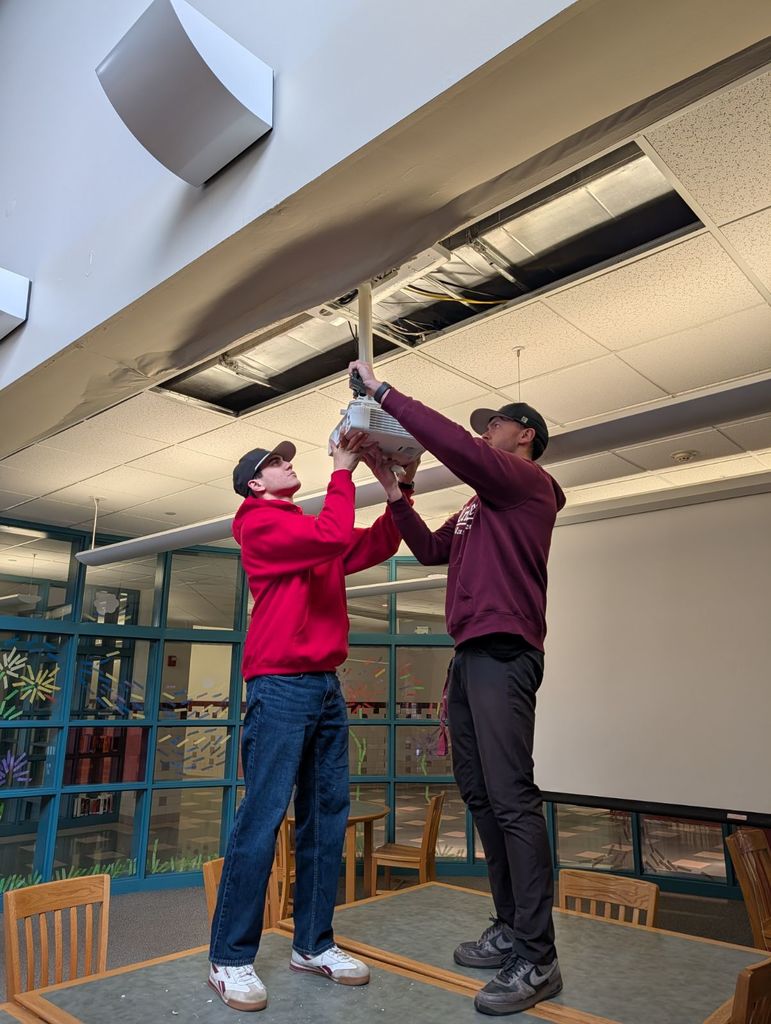 A student and tech support person install a ceiling mounted projector in the library. 