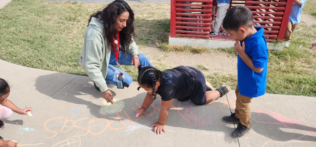 A teacher and children writing with chalk on the ground.