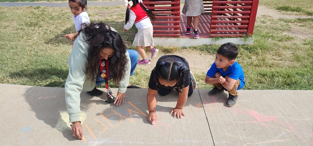 A teacher and children writing with chalk on the ground.