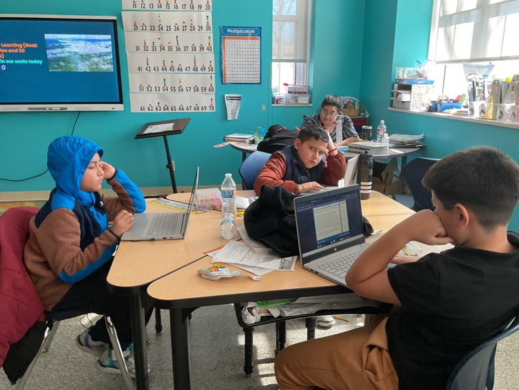 students sitting on their tables looking at a computer, reading.