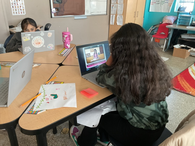 students sitting on their tables looking at a computer reading.