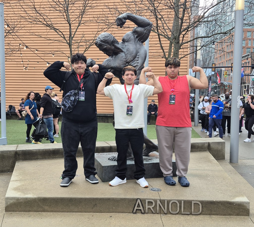 three students posing in front of a statue