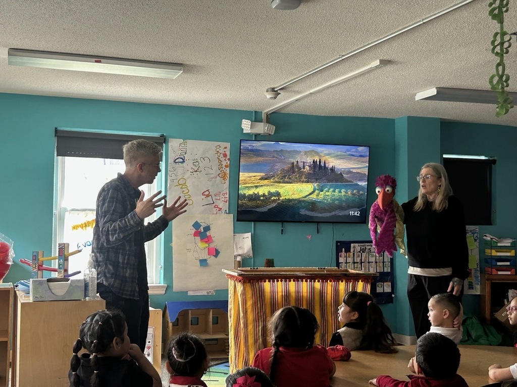 Students sitting in their classroom, attentive to a puppet presentation