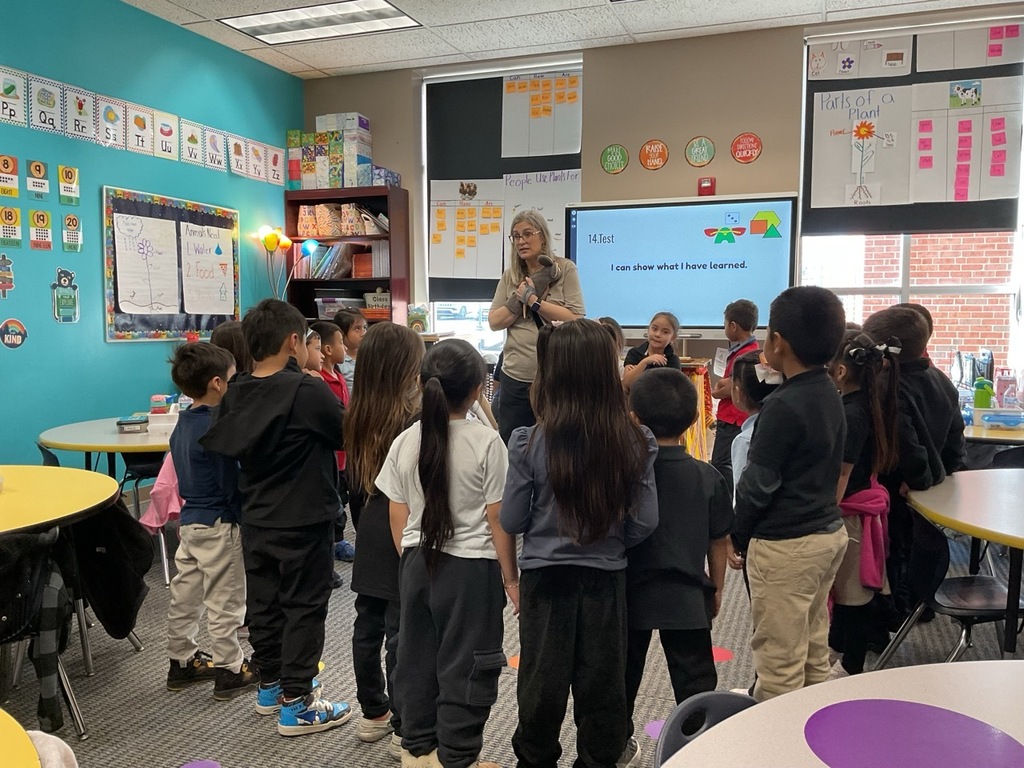 Children in the classroom standing in a circle and participating in a puppet activity