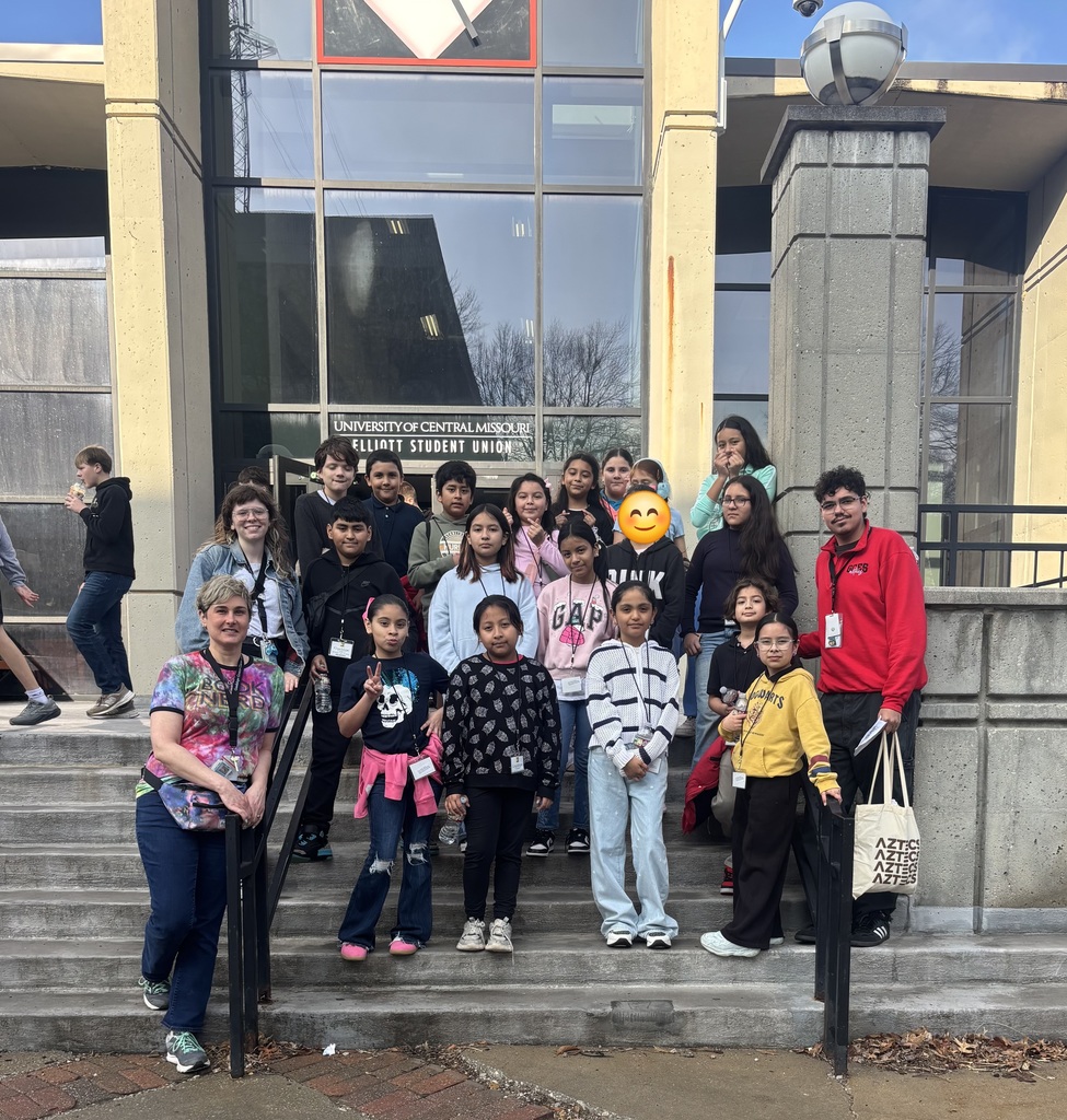 Teachers and students posing for a photo in front of a university building.
