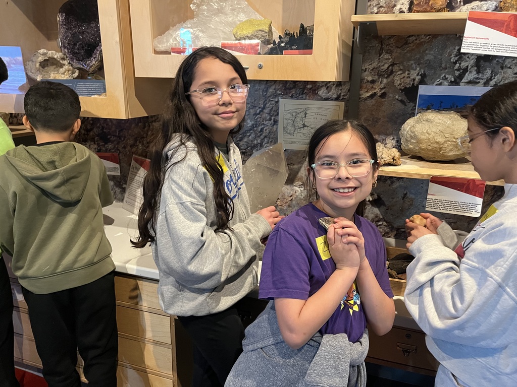 2 students looking at the camera with a background of rocks and fossils .
