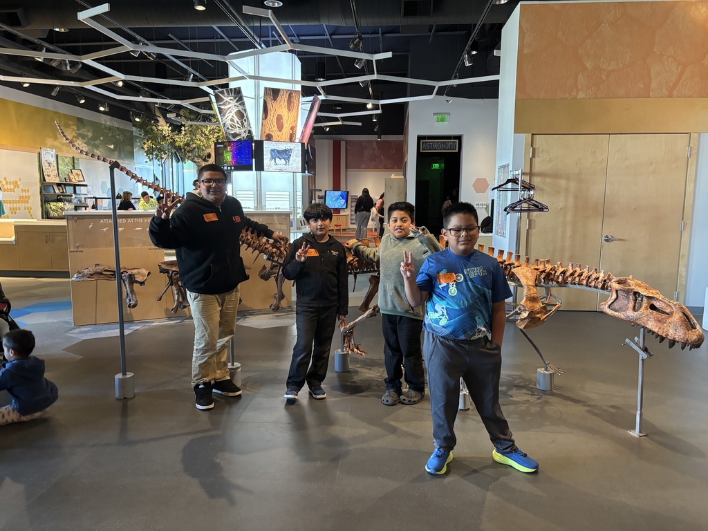 4 Students  posing for a picture with a dinosaur skeleton 