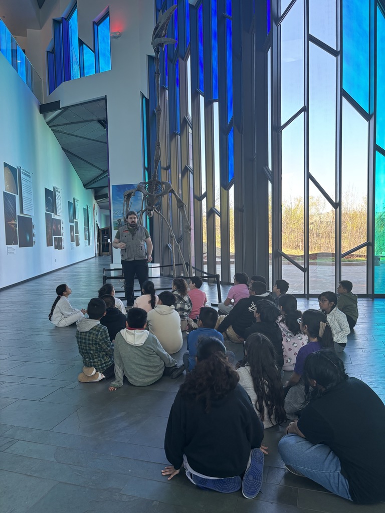 Students sitting and one adult presenting in the museum 