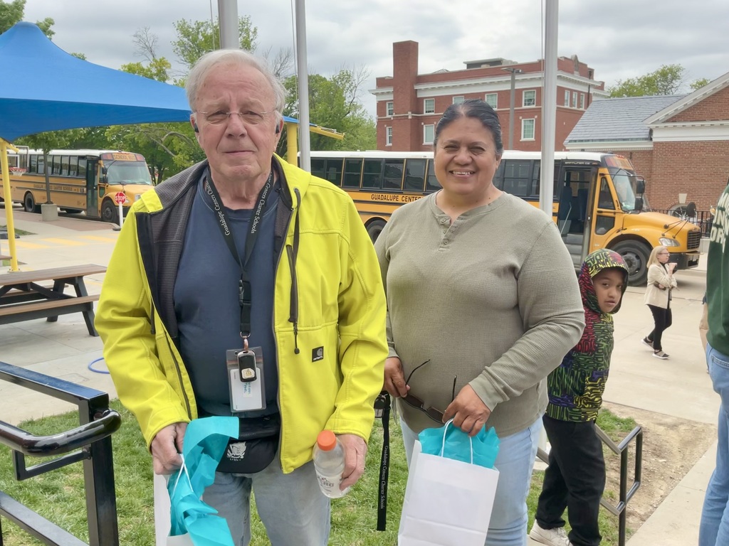 Two people holding a gift near the school bus.