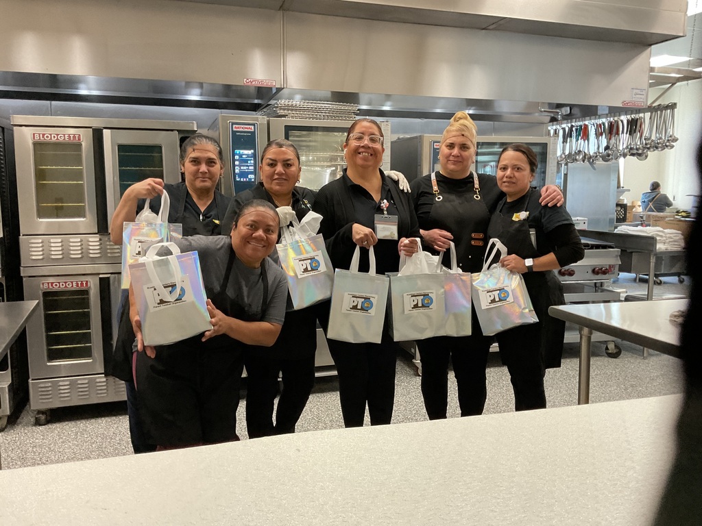 A group of cafeteria ladies smiling to the camera with an appreciation gift.