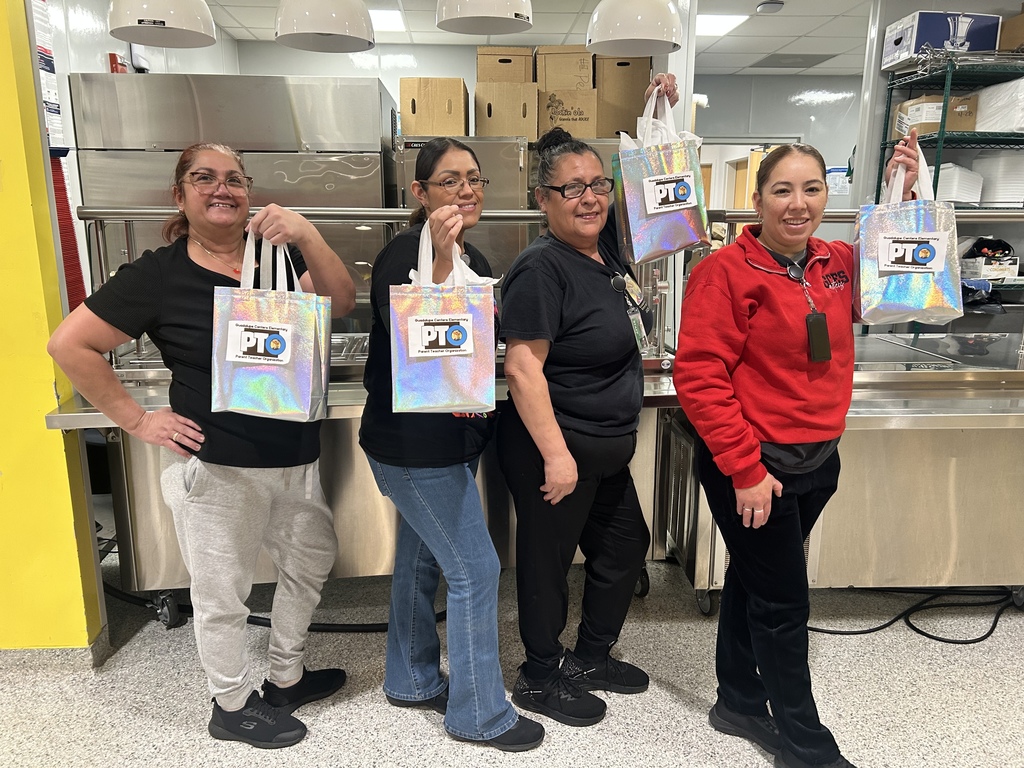 Four cafeteria ladies smiling to the camera with an appreciation gift. 