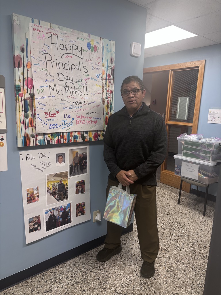 A male principal standing outside his office with an appreciation gift in front of  a big poster note from students. 