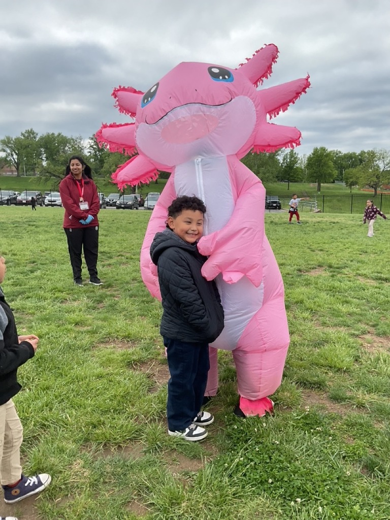 An axolotl mascot hugging a child during a picnic day, with the child happily enjoying the special moment