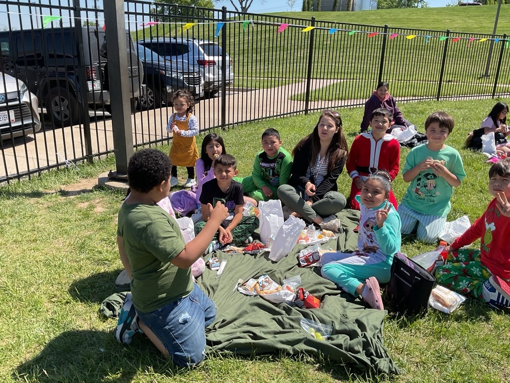 Children sitting outdoors, eating their lunch bags during a family day.