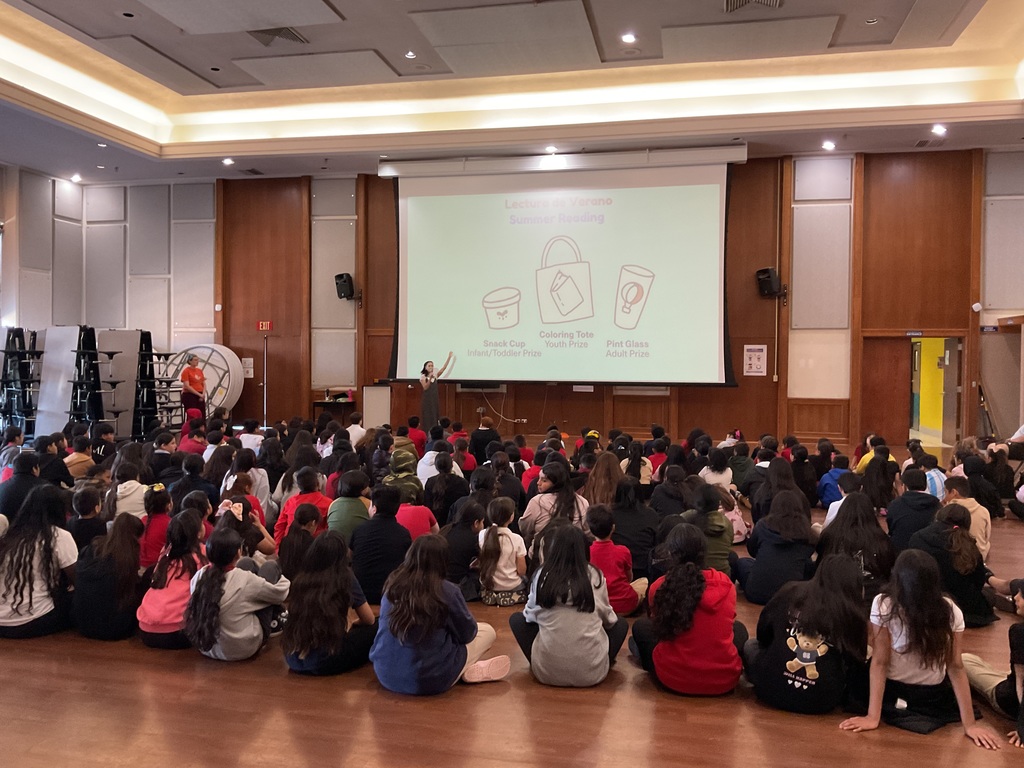 A group of students sitting on the floor looking at a big screen.
