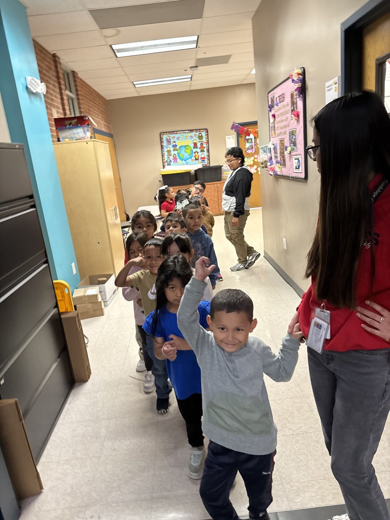 A teacher holding a students' hand while a line of students follows.