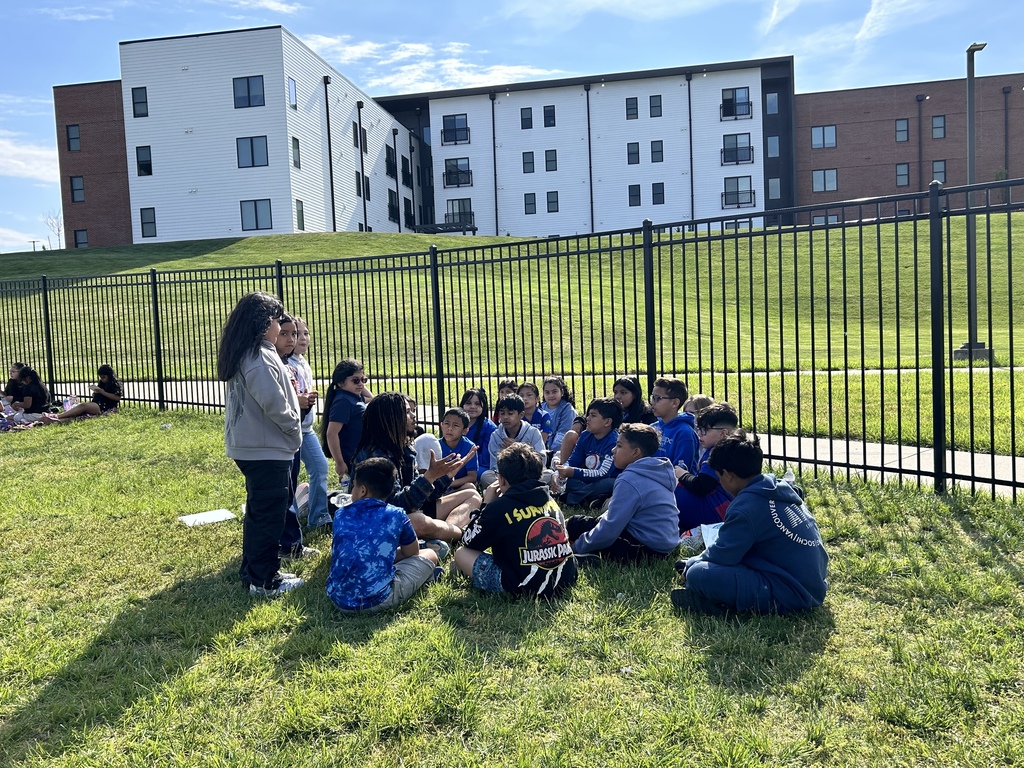 Students sitting on the grass while 2 are standing up 
