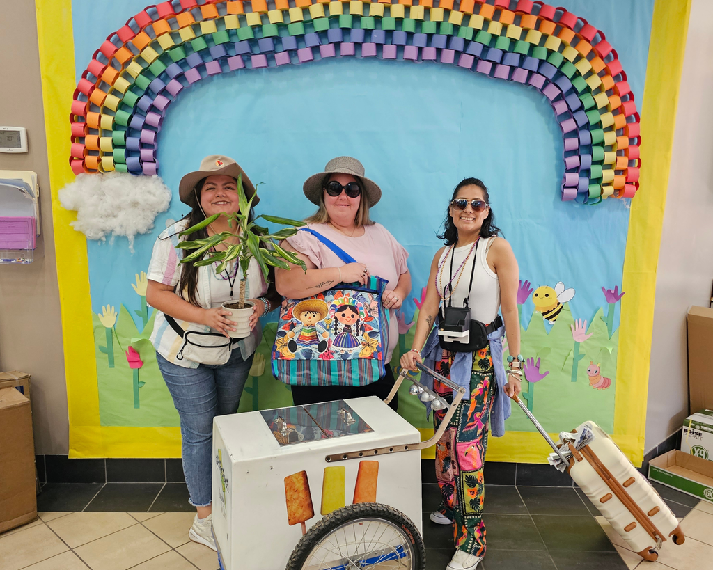 Photo of three women in a school setting dressed as tourists for a spirit week theme. They are wearing typical tourist outfits such as Hawaiian shirts, sun hats, sunglasses, and carrying cameras or maps.