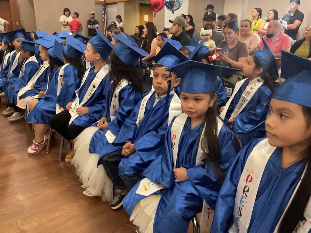 Children sitting in rows, Pre-K graduates wearing blue caps and gowns