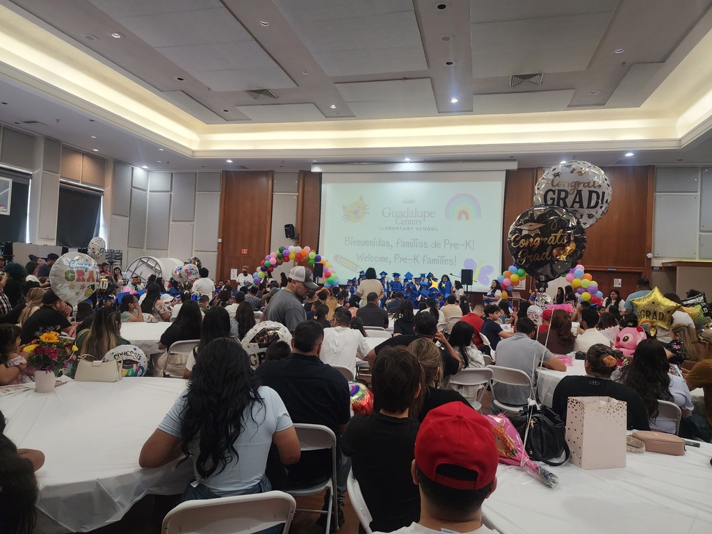 Pre-K families and students celebrating the graduation of Pre-K students in a crowded venue with balloons and decorations.