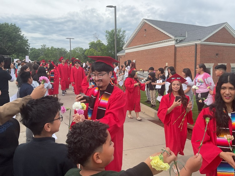 students walking wearing caps and gowns student offering a carnation