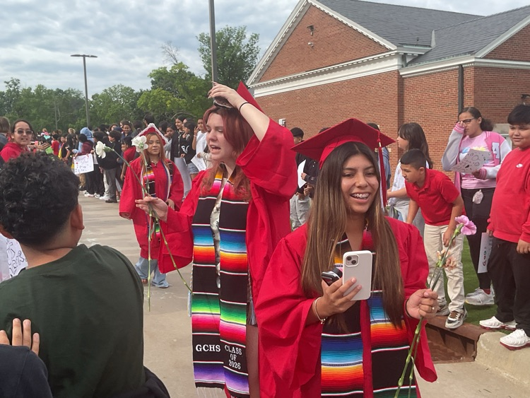 girls holding a phone and a flower in a red cap and gown