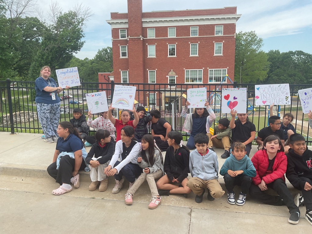 Students sitting on the sidewalk holding signs one adult standing with a sign