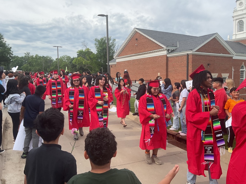 students walking wearing red caps and gowns