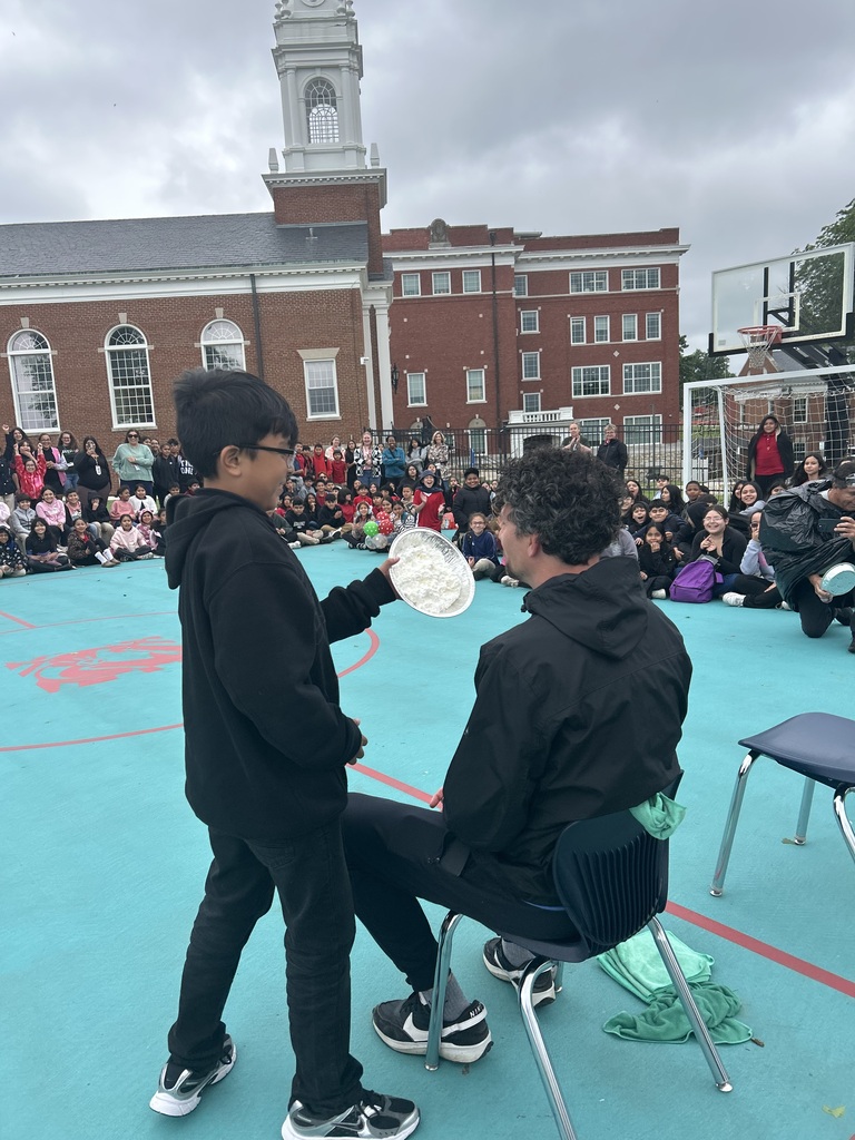 Student putting the whipped cream plate up near a sitting teacher