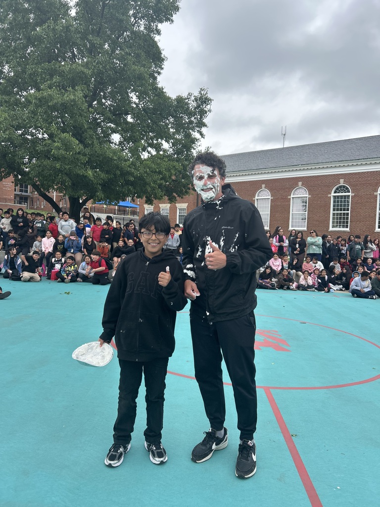 Student holding a plate and teacher with cream on face posing for the camera