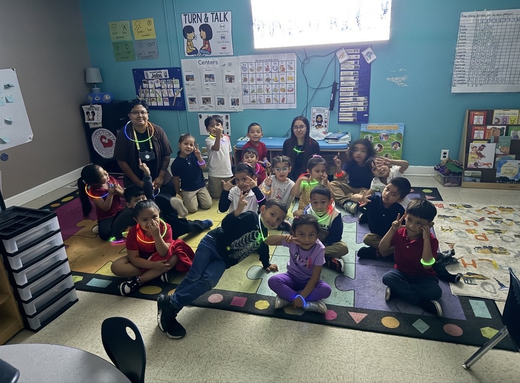 kids and teacher sitting on the floor with glow sticks looking at the camera for group picture