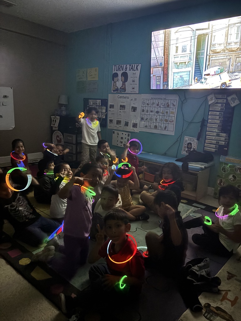 some kids sitting on the floor, others standing while watching a movie with glow sticks