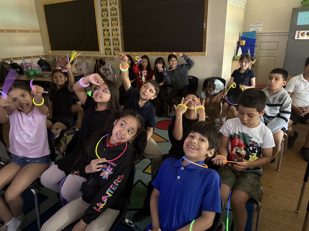 a class of students sitting on chairs while showing off their glow sticks.