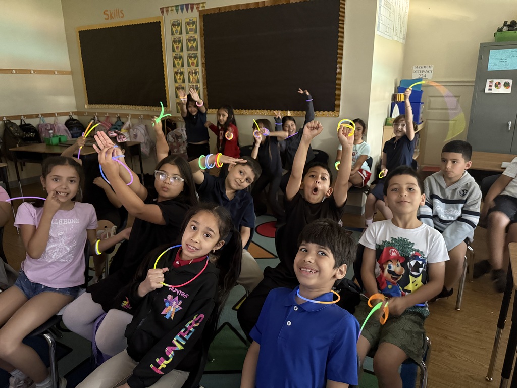 a class of students sitting on chairs while showing off their glow sticks.