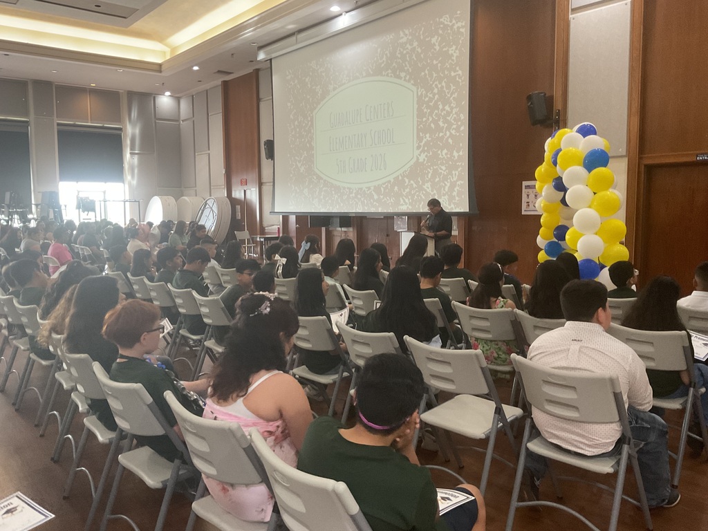 The back of a group of students sitting on chairs looking at the adult in the front