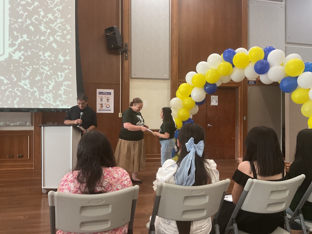 A man on a podium with a microphone, a woman handing a certificate to a student