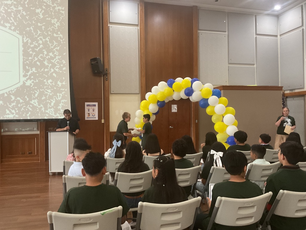 A man on a podium with a microphone, a woman handing a certificate to a student