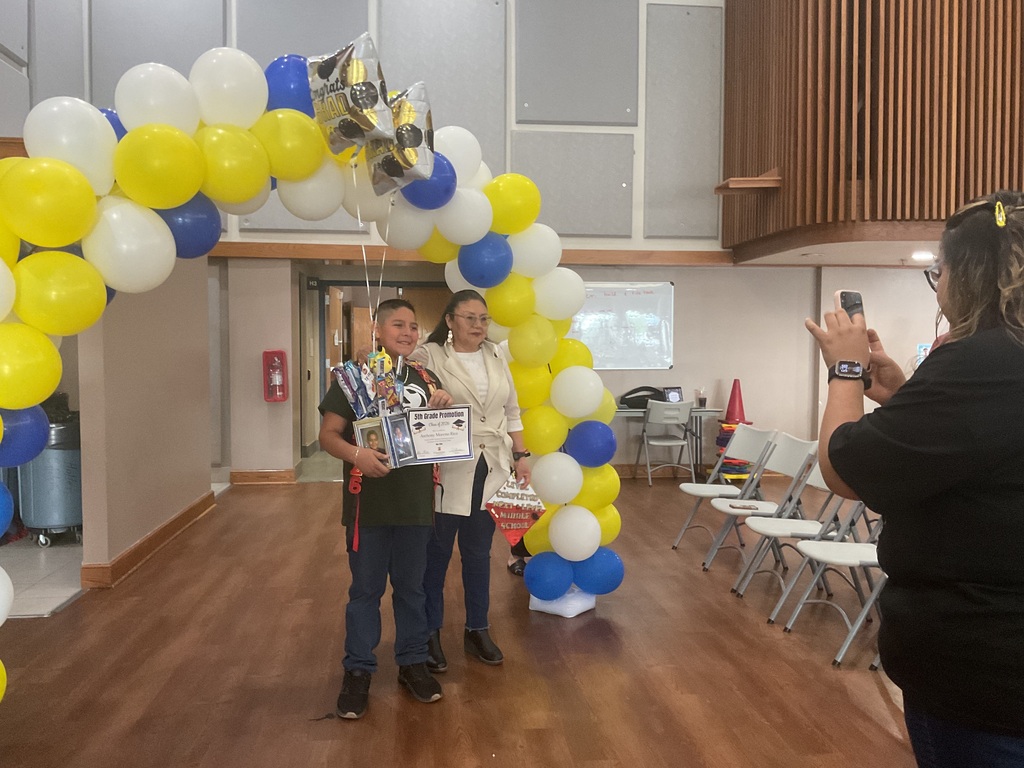 student and mother under a balloon arch posing for a picture while another adult is taking a picture