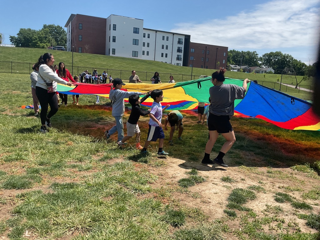 A group of student and adults holding a big parachute