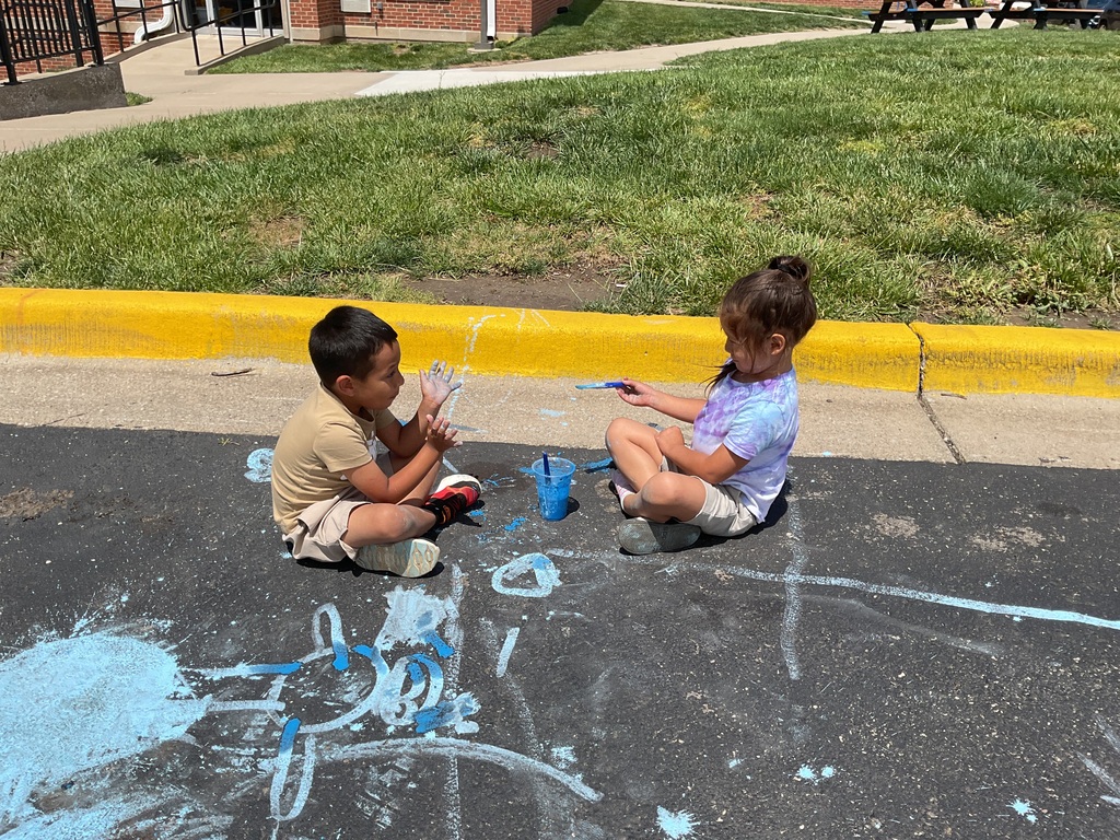 2 kids sitting on the ground facing each other and playing with paint