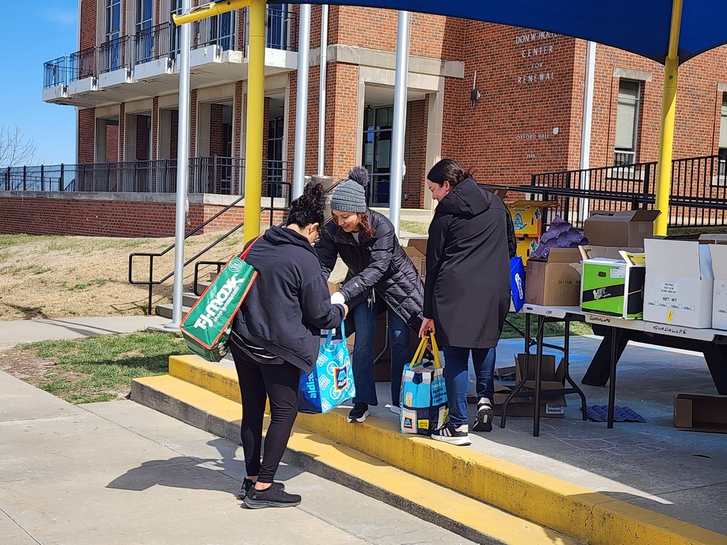 A female volunteer is distributing food during a food pantry day. She hands out food items to people in need in an organized and respectful manner as part of a community food distribution event.