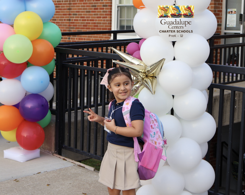 Student making a peace sign infront of a arch of balloons for a picture