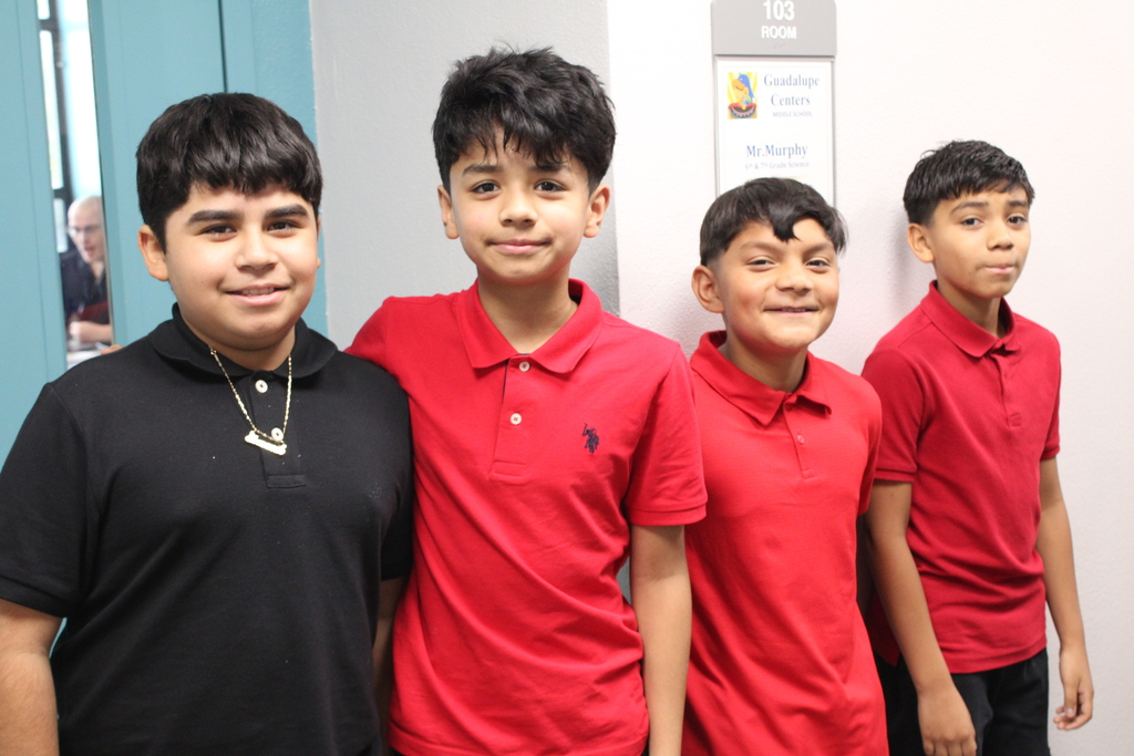 boy in black shirt and boys in red shirt posing for the camera and standing in front of a classroom 